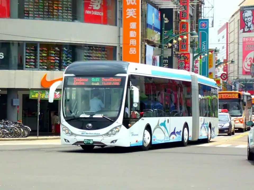 塔木德酒店評價：台中市街頭行駛中的公車，車身為白底藍色線條與海豚圖樣，背景可見Nike與New Balance運動用品店、招牌林立的商圈街景，以及行人與車輛往來的熱鬧景象。
