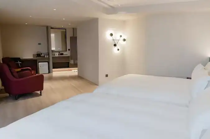 塔木德酒店評價：塔木德酒店寬敞雙床客房，採用柔和燈光與極簡設計風格，房內設有雙人床、紅色單椅與迷你吧台，整體空間明亮舒適，展現現代感與放鬆氛圍。