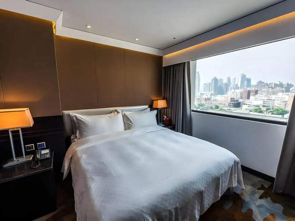 台中商旅客房大床與大面窗景，床側設有閱讀燈與木質邊桌