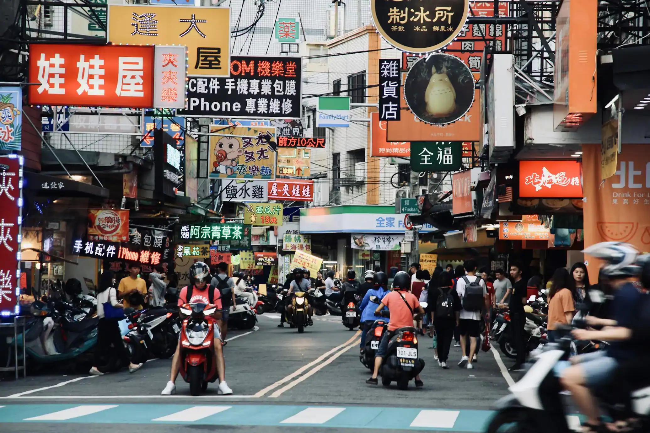 逢甲夜市街景畫面，街道兩側招牌密集且人潮眾多，機車與行人交錯呈現熱鬧市集氛圍，是選擇逢甲附近住宿旅客最期待的夜生活體驗之一。