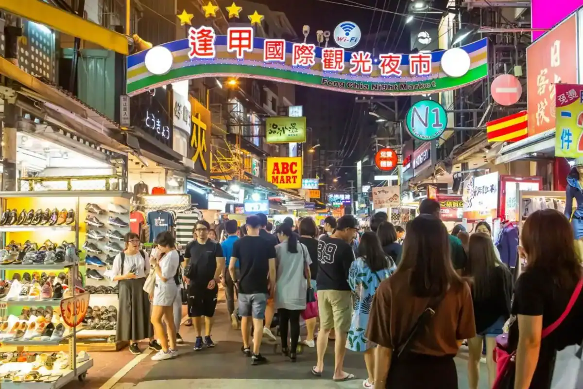 逢甲國際觀光夜市入口夜間街景畫面，人潮絡繹不絕、招牌燈光閃爍熱鬧非凡，兩側商店與美食攤位林立，是規劃逢甲夜市附近住宿時最受旅客關注的熱門地標商圈。