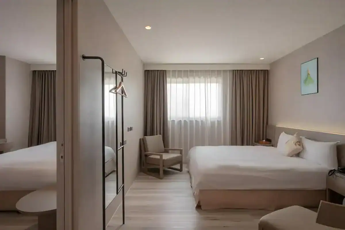 享得道 HOTEL 客房空間設計,房內設有雙人床、單椅與大面窗簾採光,整體以簡約木質與淺色系裝潢呈現,是台中逢甲飯店常見的舒適住宿房型。