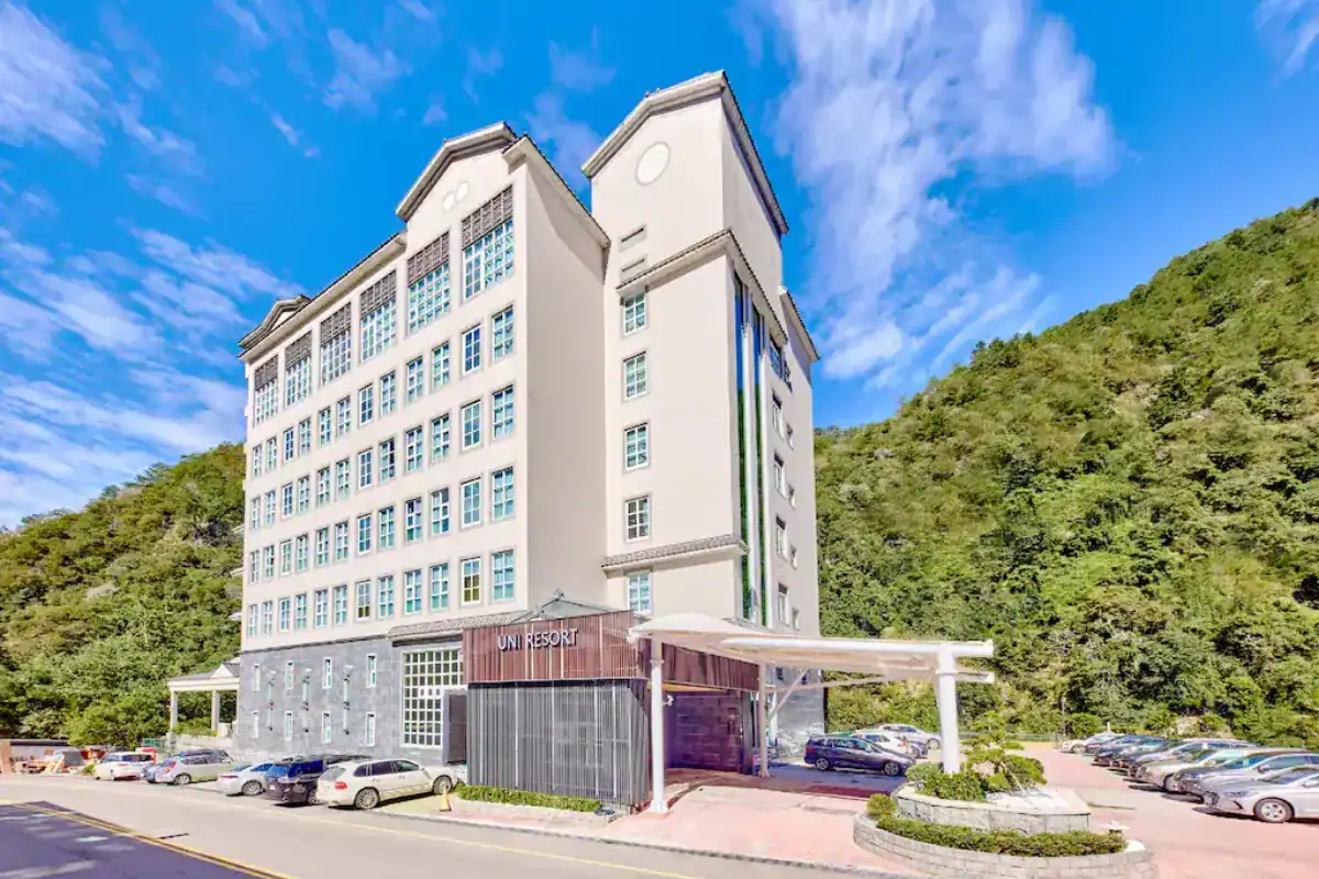 統一渡假村谷關溫泉養生會館外觀建築，白色多層飯店坐落於山林之中，前方設有停車空間，呈現適合親子入住的谷關住宿選擇。