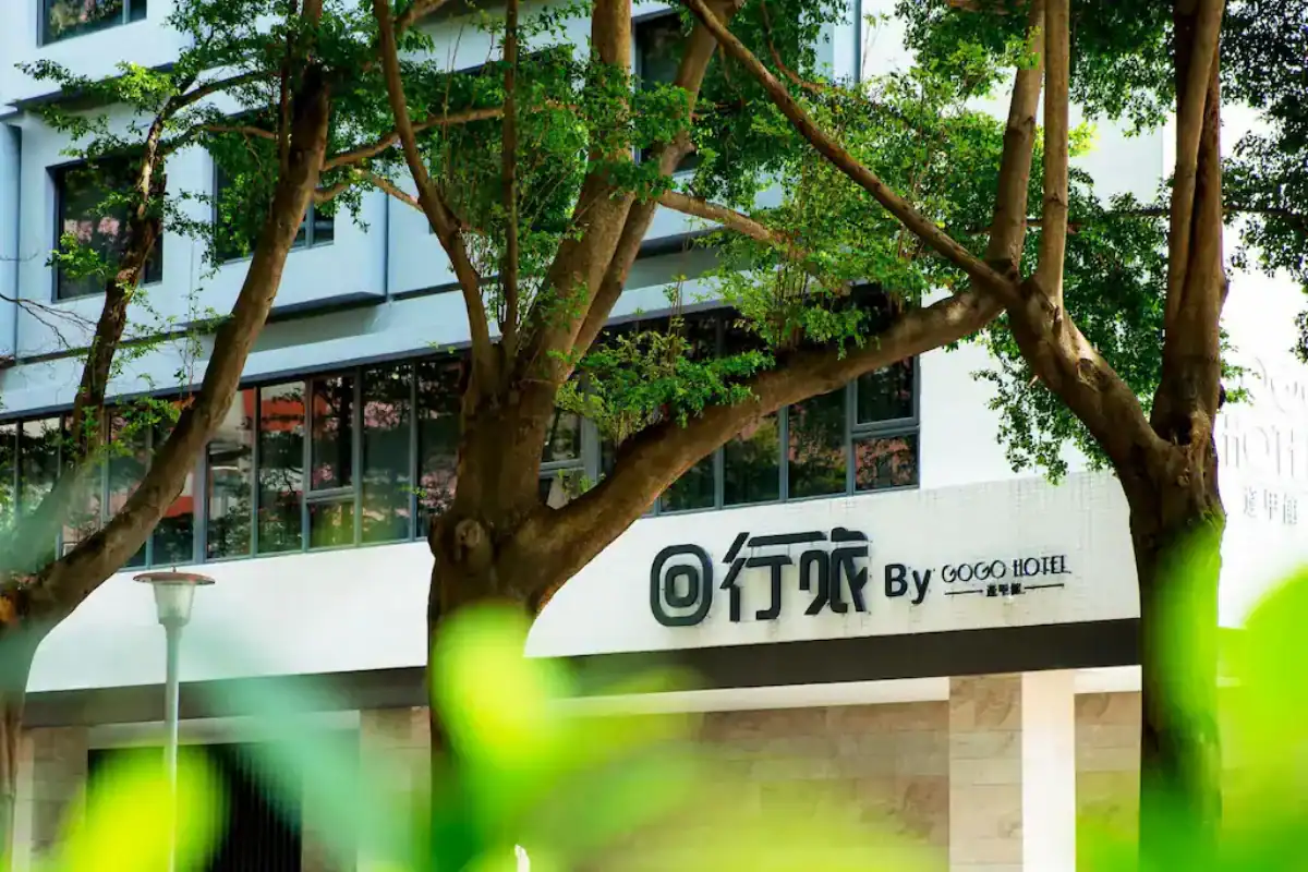 GOGO HOTEL 逢甲館外觀建築被綠樹環繞,白色牆面上可見飯店招牌,是台中逢甲飯店住宿選擇之一。