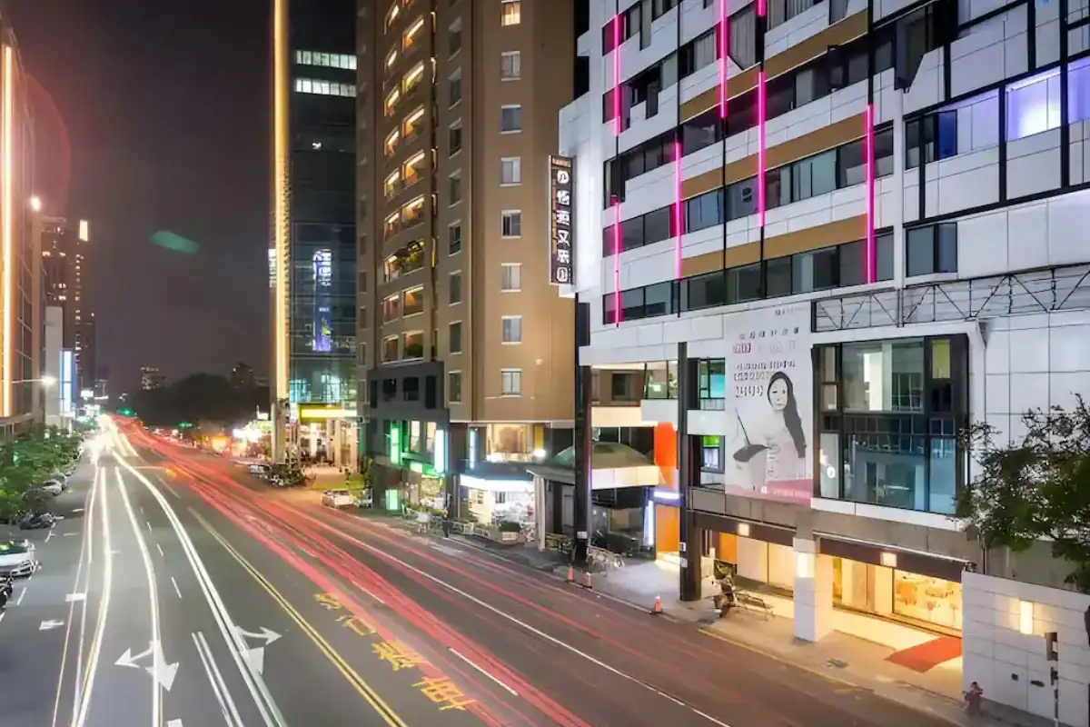 台中西區住宿：飯店外觀夜景，建築燈條映照街道車流，展現台中市區熱鬧氛圍