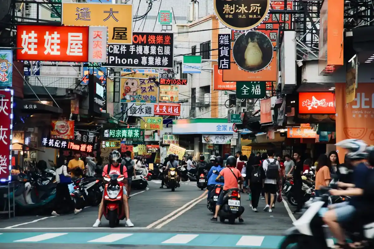 逢甲夜市街景畫面，街道兩側招牌密集且人潮眾多，機車與行人交錯呈現熱鬧市集氛圍，是選擇逢甲附近住宿旅客最期待的夜生活體驗之一。